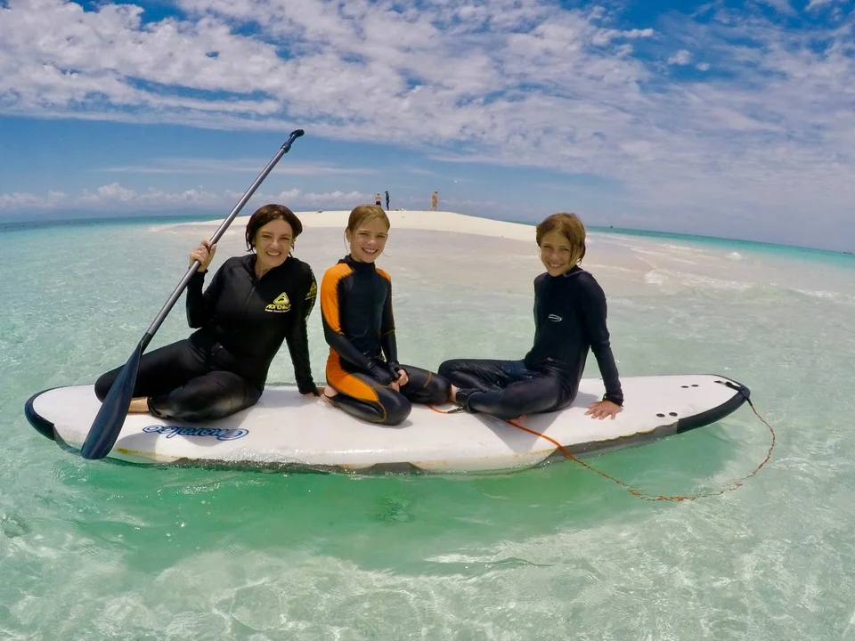 Guests sharing a paddleboard in shallow water